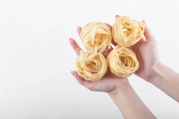 istock Female hands holding tagliatelle nests on white background 1302991357