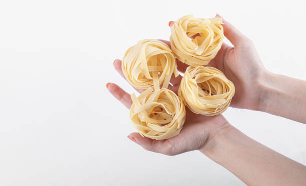 Female hands holding tagliatelle nests on white background