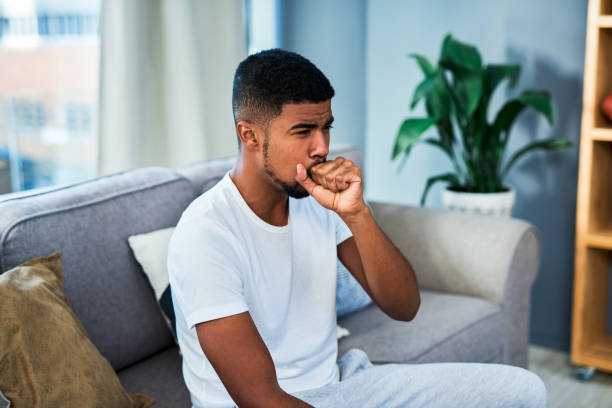 The pain worsens when I cough Shot of a young man coughing while sitting on a sofa at home male chest pain stock pictures, royalty-free photos & images