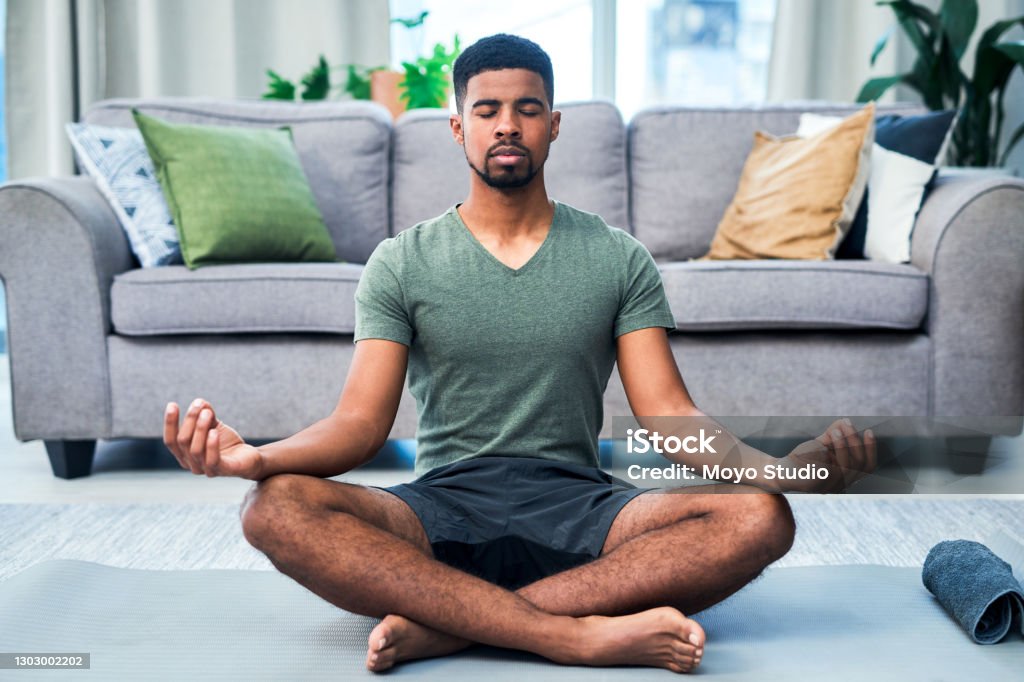 My presence is my power Shot of a young man meditating at home Meditating Stock Photo