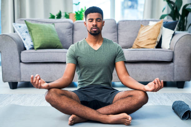 My presence is my power Shot of a young man meditating at home mindfulness photos stock pictures, royalty-free photos & images