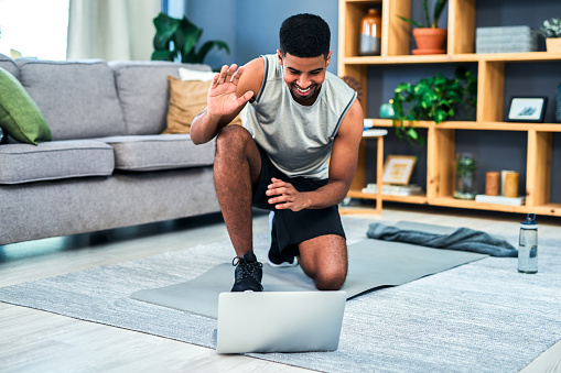 Shot of a young man using a laptop while exercising at home
