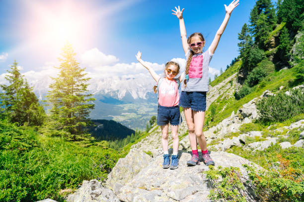 les filles randonnée sur la belle journée d’été dans les alpes montagnes autriche, se reposant sur le rocher et admirer une vue imprenable sur les sommets des montagnes. loisirs de vacances en famille actifs avec les enfants. activités amusantes et  - european alps mountain mountain peak rock photos et images de collection