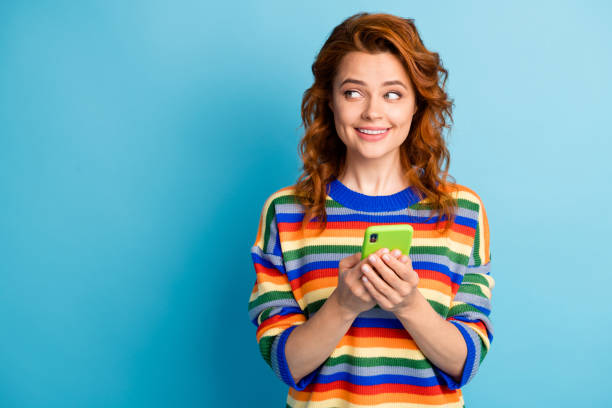 istock Photo of cute shiny lady dressed striped pullover holding gadget looking empty space isolated blue color background 1303005058