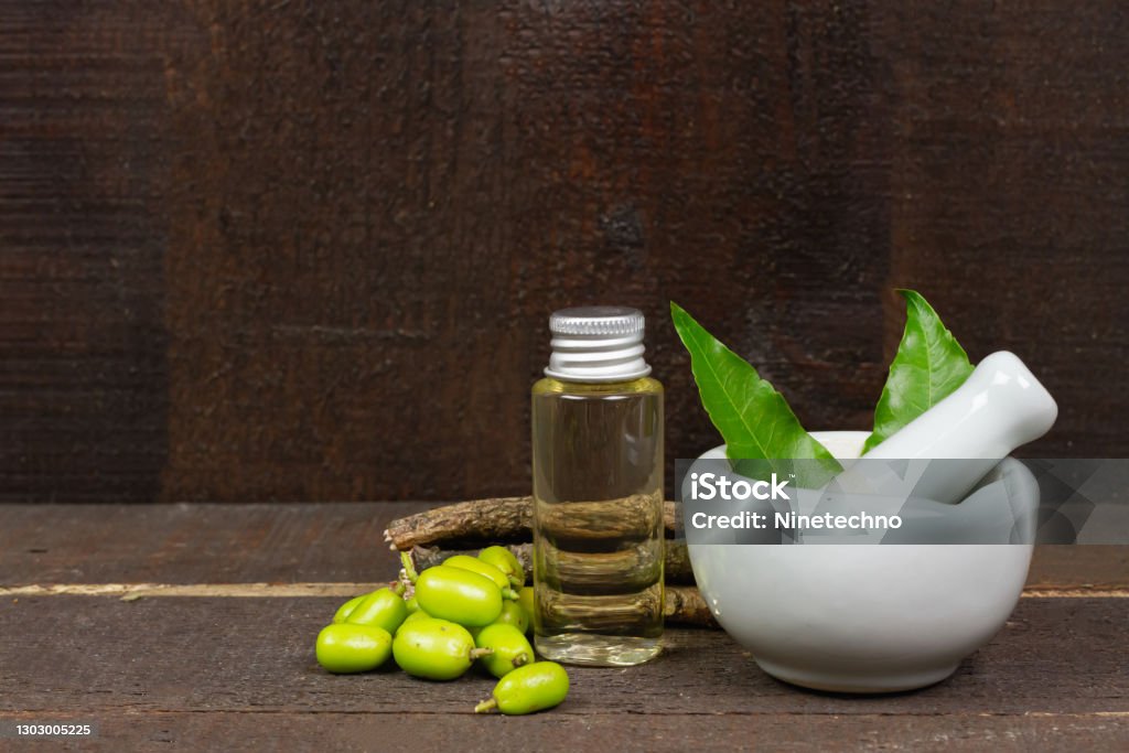 Neem oil in bottle and Neem leaf in mortar and pestle Neem oil in bottle and Neem leaf in mortar and pestle white ceramic with stick and fruit on wooden background. Neem Tree Stock Photo