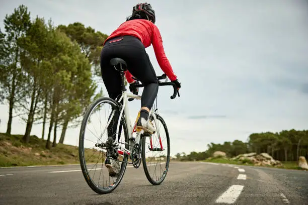 Low angle rear view of mature sportswoman cycling uphill past camera on Cap De Creus peninsula road near Mediterranean.