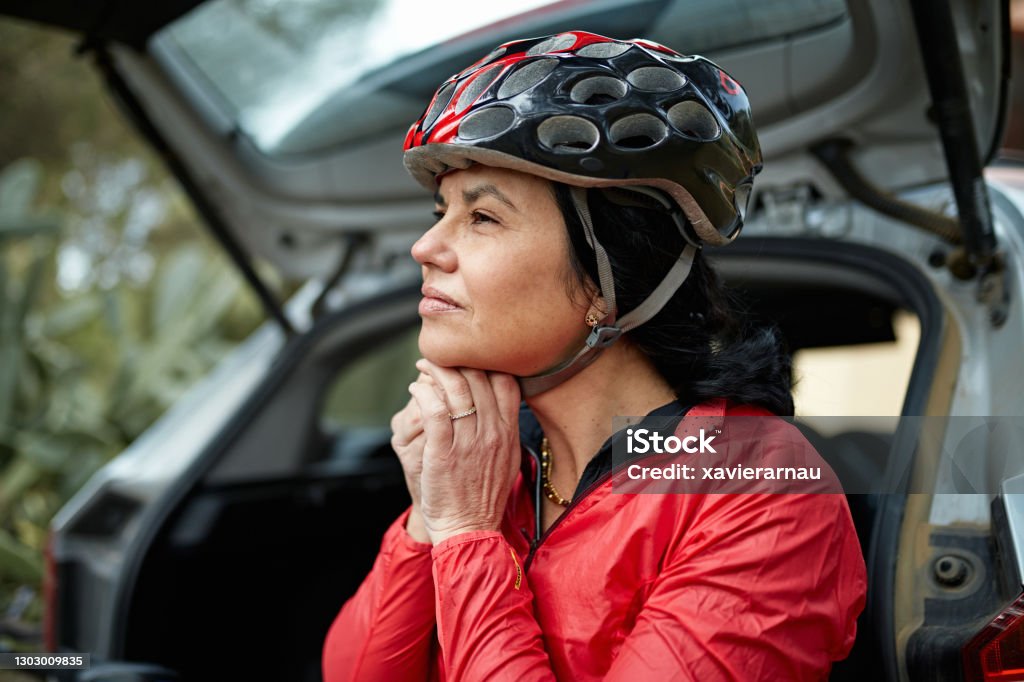 Early 50s Female Athlete Putting on Cycling Helmet Partial view of Hispanic woman wearing sports clothing and tightening strap on helmet as she prepares for workout. Cycling Helmet Stock Photo