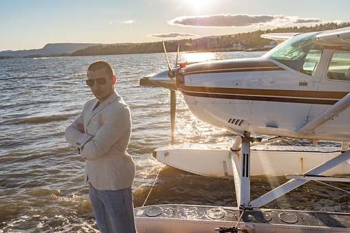Young male standing next to the water airplane at sunset.