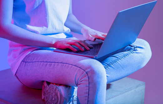 Remote online education and work, modern employer and urgent task during covid-19 lockdown. Busy teen lady in casual, sitting and typing in laptop, in neon, studio shot, cropped, free space, close up