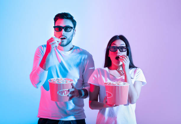 Amazing entertainment, leisure time together and cinema with modern technology Amazing entertainment, leisure time together and cinema with modern technology. Surprised calm young guy and lady in 3d glasses eating popcorn and watching movie, in neon, studio shot, free space 3 d glasses stock pictures, royalty-free photos & images