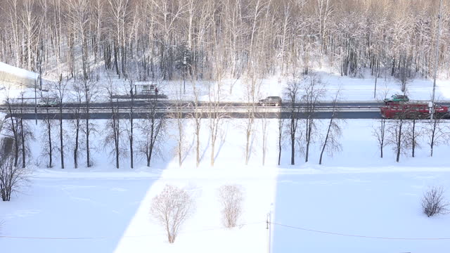 cars, trucks, ambulance go on the road, highway in winter, against the background of snow and forest, shooting from above, sun rays