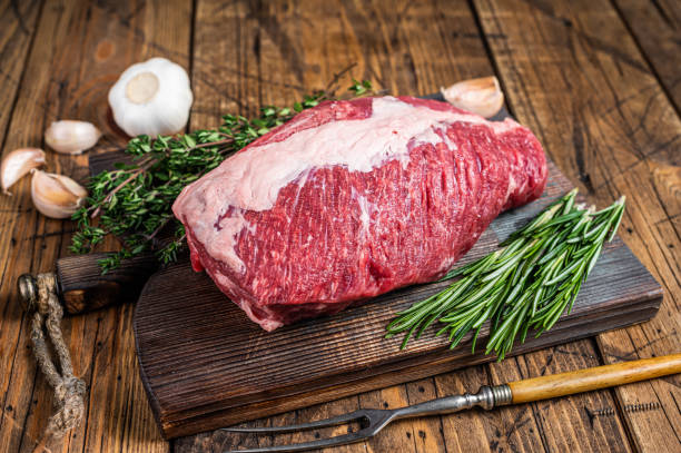 carne de res cruda fresca cortada en una tabla de madera con hierbas. fondo de madera. vista superior - round of beef fotografías e imágenes de stock