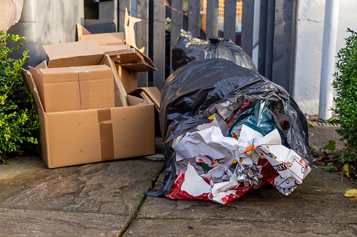 Christmas household waste consisting of boxes and wrapping paper, beside a bin or trash can in a garden