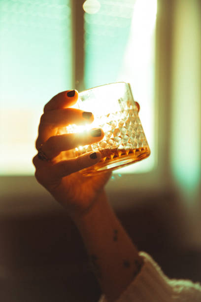 de hand die van vrouwen een alcoholische drank tegen verlichte zon houdt - alcohol drinks stockfoto's en -beelden