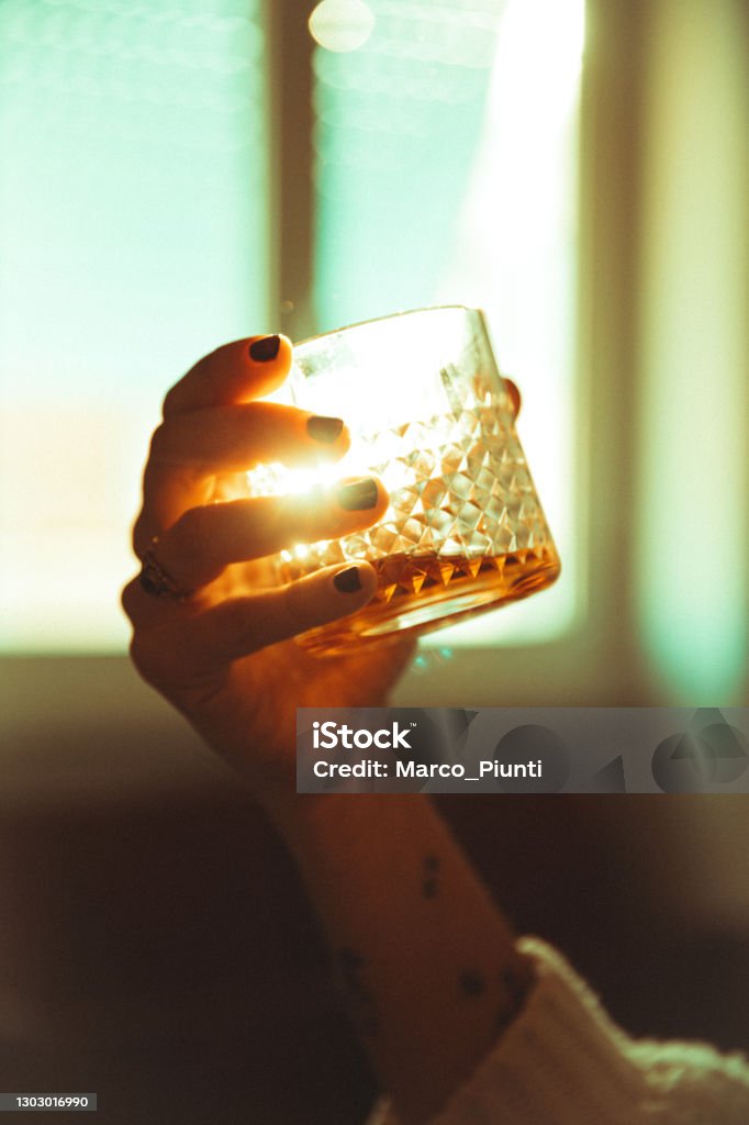 Women hand holding an alcoholic drink backlit sun Whiskey Stock Photo