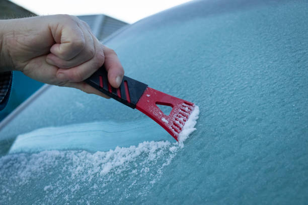 A man scraping ice off a frozen wind shield or screen of a vehicle on a cold winters morning stock photo