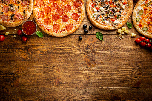 Flat-lay of different types of pizza and red wine over rustic wooden table, top view. Fast food lunch, celebration, pizza party