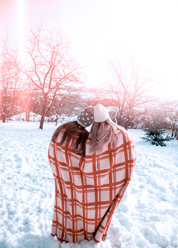 Rear view of Two Women in embrace in Winter snow scene outdoors.