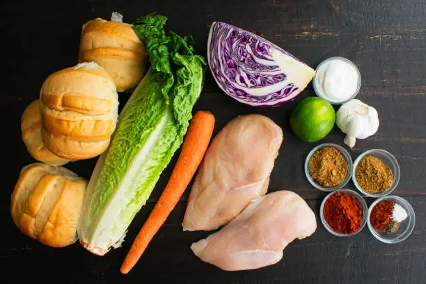 Raw chicken, fruits, vegetables, and spices used to make spicy grilled chicken sandwiches