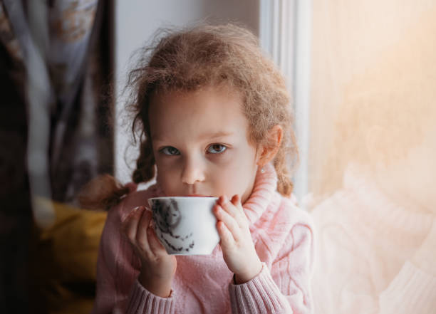 istock Little girl drinks from a cup by the window 1303025692