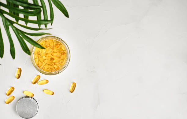 Fish oil capsules with omega 3 and vitamin D in a glass jar on a white concrete table top view, healthy eating concept. Cod liver oil softgels, layout with copy space stock photo