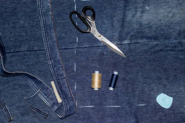Making new handmade clothes from old ragged jeans: ripped trouser-leg, threads, scissors and chalk. Concept of things reuse and natural resources preserving.