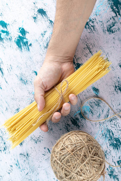 istock Male hand holding spaghetti pasta on colorful surface 1303035970