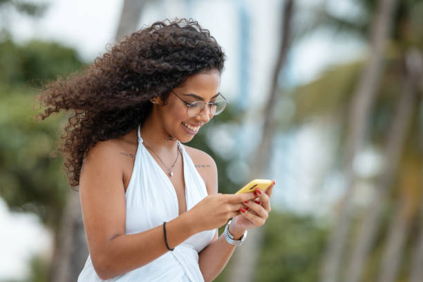 ビーチでスマートフォンを持つ若い女性 - 混ぜる ストックフォトと画像