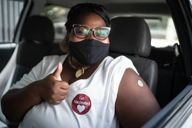 porträt einer glücklichen frau in einem auto mit einem "get geimpft" aufkleber - tragen gesichtsmaske - daumen hoch fotos stock-fotos und bilder