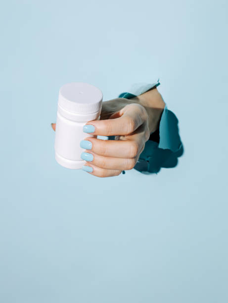 istock Female hand holding pill bottle breaking through pastel blue wall 1303040104