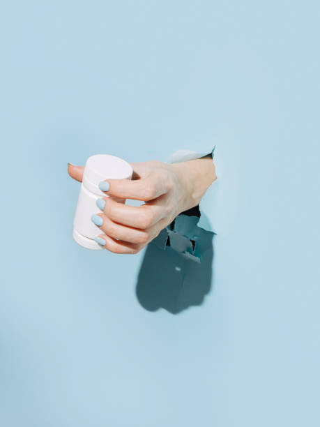 istock Female hand holding pill bottle breaking through pastel blue wall 1303040121