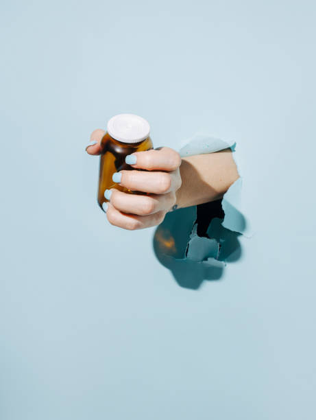 Female hand holding bottle breaking through pastel blue wall