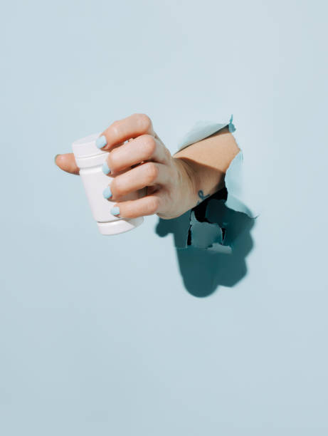 istock Female hand holding pill bottle breaking through pastel blue wall 1303040303