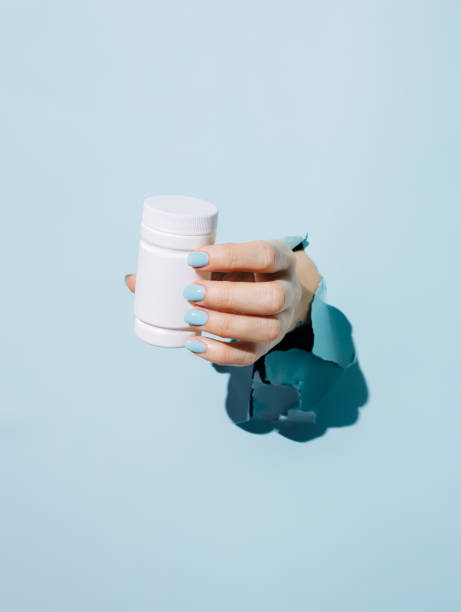istock Female hand holding pill bottle breaking through pastel blue wall 1303040415