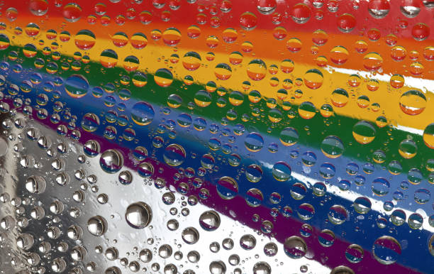 istock Rainbow. Multicolored drops of water are located against a mirror background with strips of rainbow colored paper. 1303041559