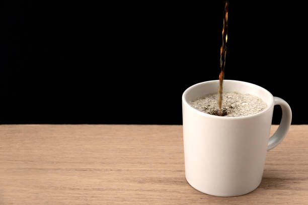 istock Fresh coffee being poured into a mug on a wood table with black background 1303042647