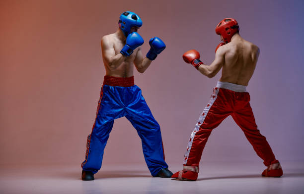 luchando contra boxeadores masculinos con cascos y guantes de boxeo en luz roja en estudio, entrenamiento de artes marciales - accesorio de cabeza fotografías e imágenes de stock