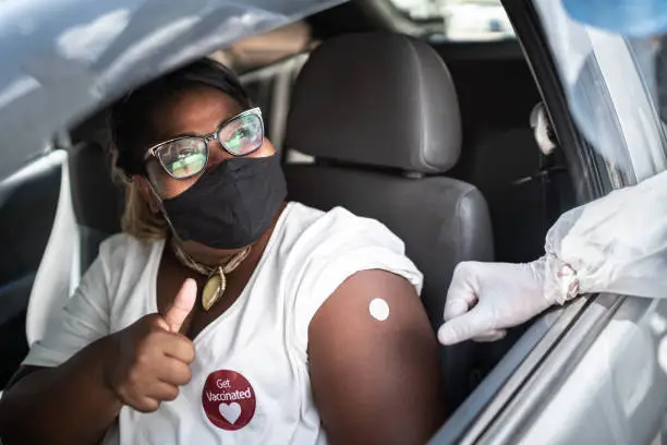 Photo of Happy woman in a car with a 'get vaccinated' sticker - wearing face mask