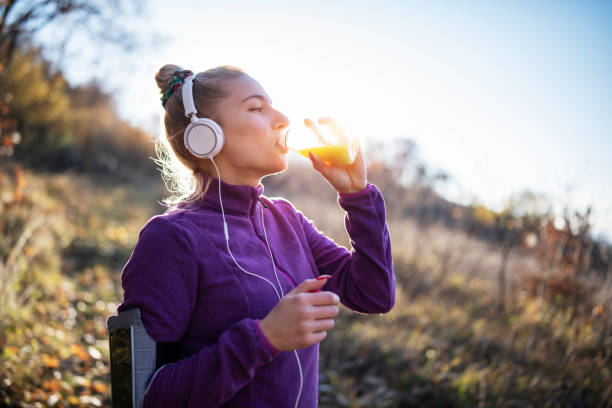 Young fit woman taking a break from jogging in the nature. Portrait of a young fit woman taking a break from running in the forest  and drinking orange juice. juice drink stock pictures, royalty-free photos & images