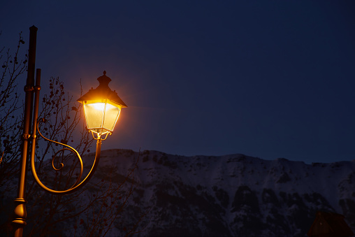 Victorian vintage antique street warm yellow light lantern at the evening with snowy alpine mountain and dark blue sky background