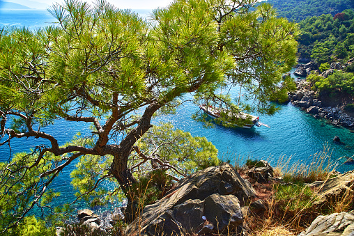 View from the mountain to the blue bay of Mediterranean Sea with yacht, rocky mountain slopes with pine-tree, near Fethiye-Turkey