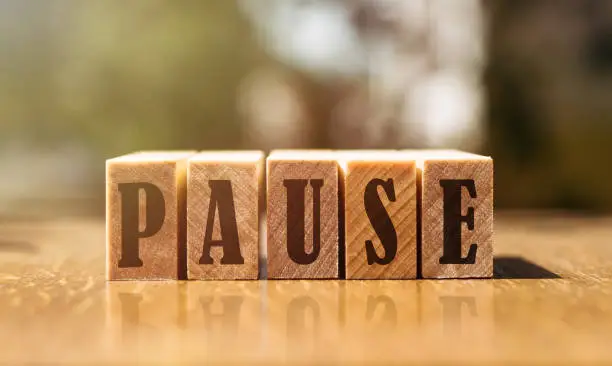 Photo of The word pause with wooden blocks on the table in the sunlight.