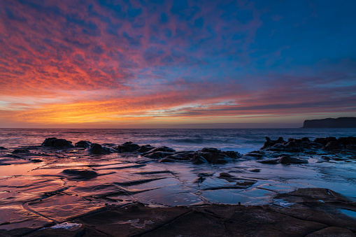 Colourful sunrise seascape with high cloud and tessellated rock platform at North Avoca Beach on the Central Coast, NSW, Australia.
