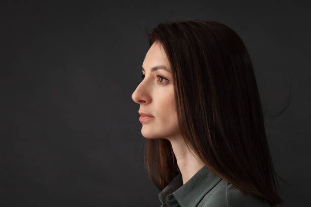 Studio portrait of attractive 38 year old woman with brown hair Close up studio portrait of attractive 38 year old woman with long brown hair in khaki green shirt on black background olive green shirt stock pictures, royalty-free photos & images