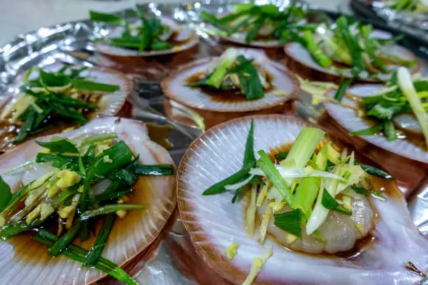 Close-up of a platter of steam cooked scallops in a special Chinese-style soy sauce and garnishes as served in Cantonese restaurants around the world. A catering concept.