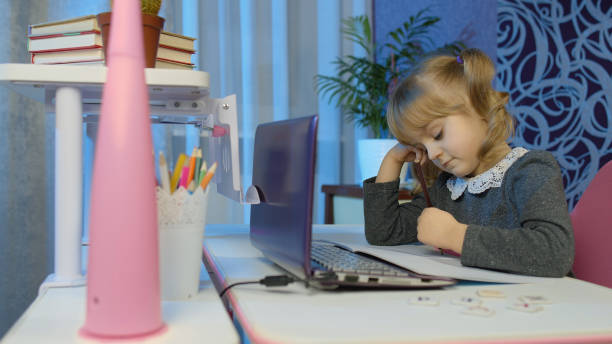 bambino annoiato che ascolta la lezione di audio studiando a tavola usando il computer portatile digitale, facendo i compiti - home schooling audio foto e immagini stock