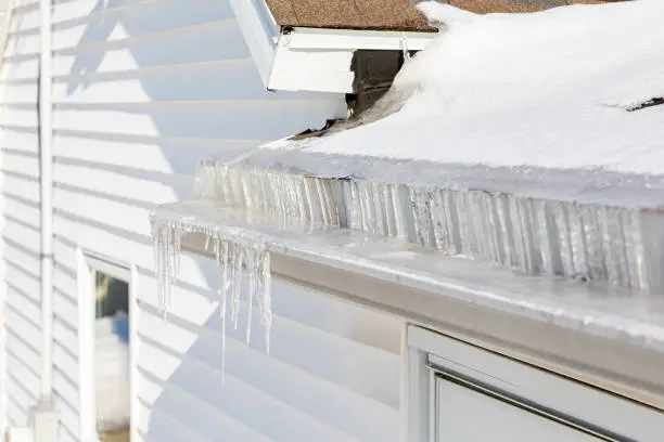 Photo of Roof gutter full of ice and icicles after winter storm. Concept of roof damage, home maintenance and repair.