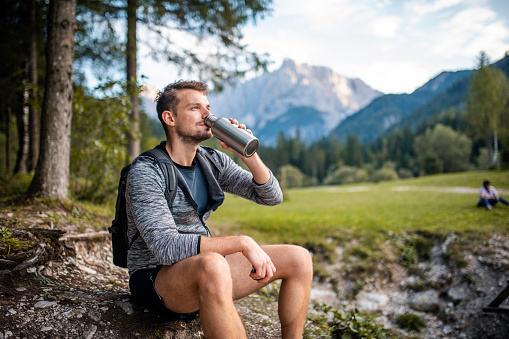 Male hiker in early 30s resting and drinking water near alpine town Kranjska Gora in northwestern Slovenia.