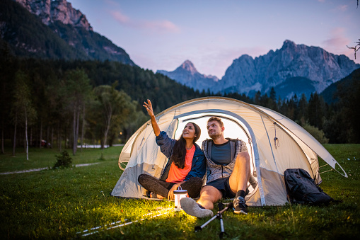 Smiling campers in 20s and 30s sitting on tent porch and admiring scenic beauty of Kranjska Gora in northwestern Slovenia.