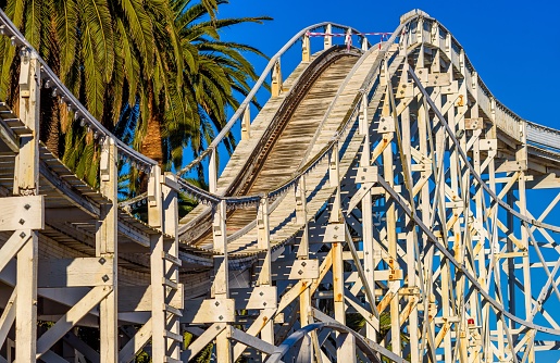 An old wooden construction rollercoaster against a blue sky and palm tree
